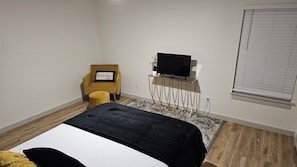 A bedroom with a bed, a chair, a television on a stand, and a window with blinds.