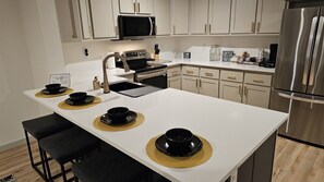 Ett modernt kök med en central köksö, vitvaror i rostfritt stål och en minimalistisk design.