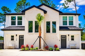 A two-story house with a brick facade, numbered 124 and 122, featuring a central palm tree and red foliage plants.