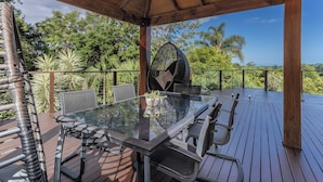 A covered outdoor dining area with a glass table and chairs, surrounded by a wooden deck and metal railings. - Ocean Shores Oasis  (Ocean Shores)