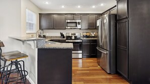 A modern kitchen with dark cabinetry, stainless steel appliances, and a wooden floor. - NEW~9 min to Dollywood~Hot Tub~Arcade~4 Bedroom (Sevierville)