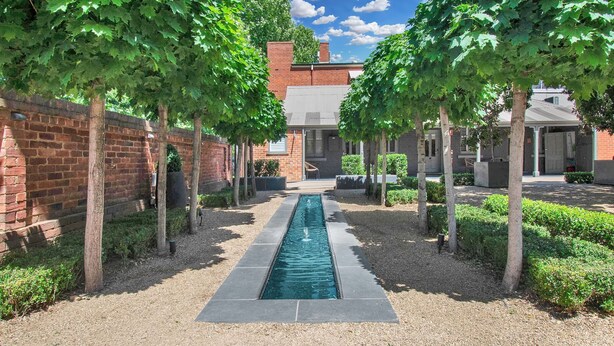 A courtyard with a central water feature, surrounded by brick walls and trees. - The Houston Boutique Hotel Wagga (Wagga Wagga)