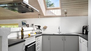 A compact kitchen with white cabinets, a built-in oven, a coffee maker, and a window above the sink. - Beautiful home in Vestervig with sauna (Vestervig)