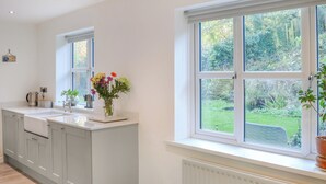 A modern kitchen with a large window, white cabinetry, and a flower vase on the counter. - Humford Mill Cottage (Humford Mill near Bedlington)