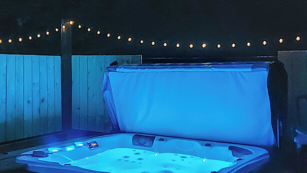 A hot tub with a canopy, surrounded by a wooden fence and string lights. - Humford Mill Cottage (Humford Mill near Bedlington)