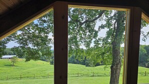 A room with large windows offering a view of a green field and trees. - Rustic Cabin on Homestead Farm (Dobson)