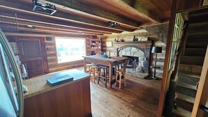A rustic cabin interior with a wooden bar, a stone fireplace, and a large window. - Rustic Cabin on Homestead Farm (Dobson)