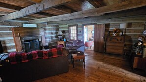 A log cabin interior with a wooden floor, a leather sofa, a fireplace, and a wooden dresser. - Rustic Cabin on Homestead Farm (Dobson)