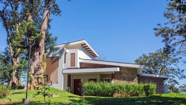 A modern two-story house with a stone facade, a large tree in the background, and a clear blue sky.