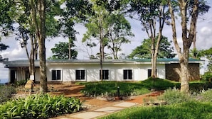 A modern two-story house with a stone foundation, surrounded by lush greenery and trees.