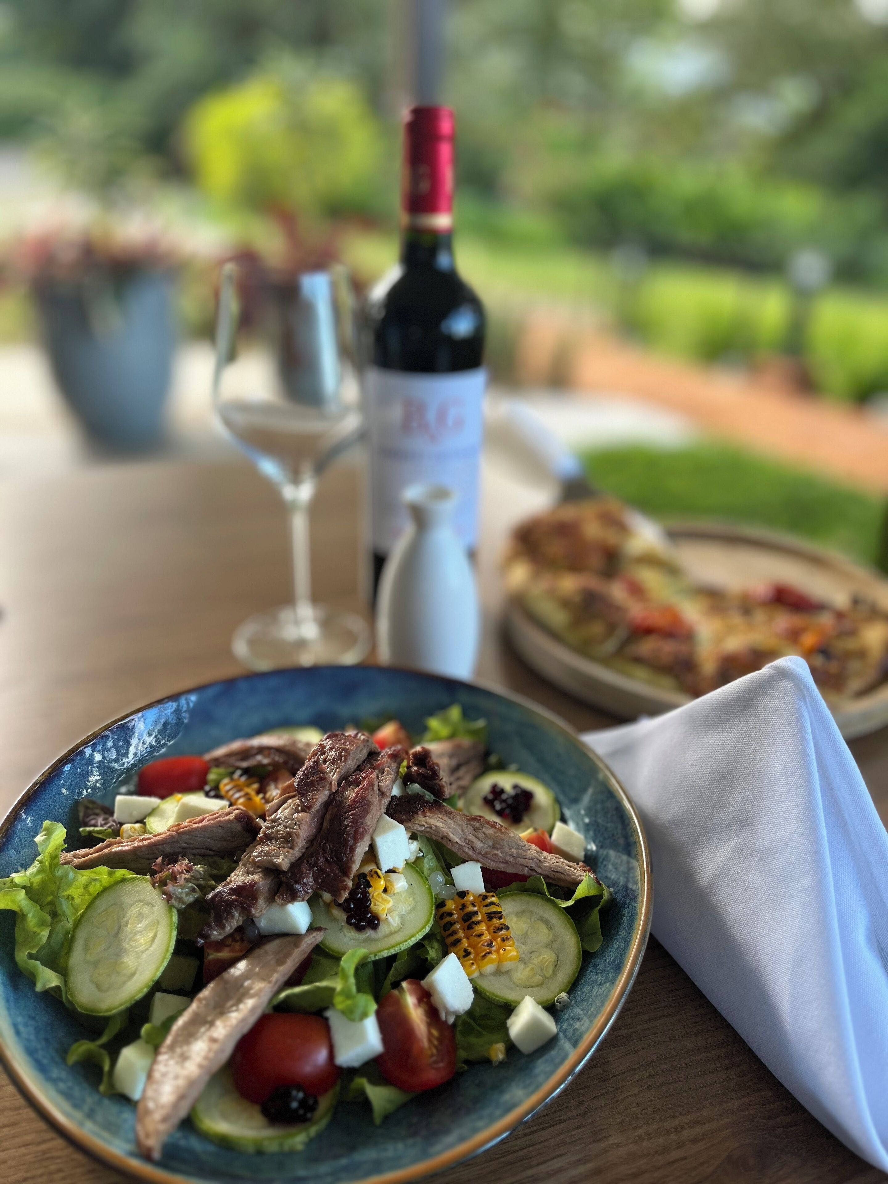 Een tafel met een salade, een fles wijn en een wijnglas.