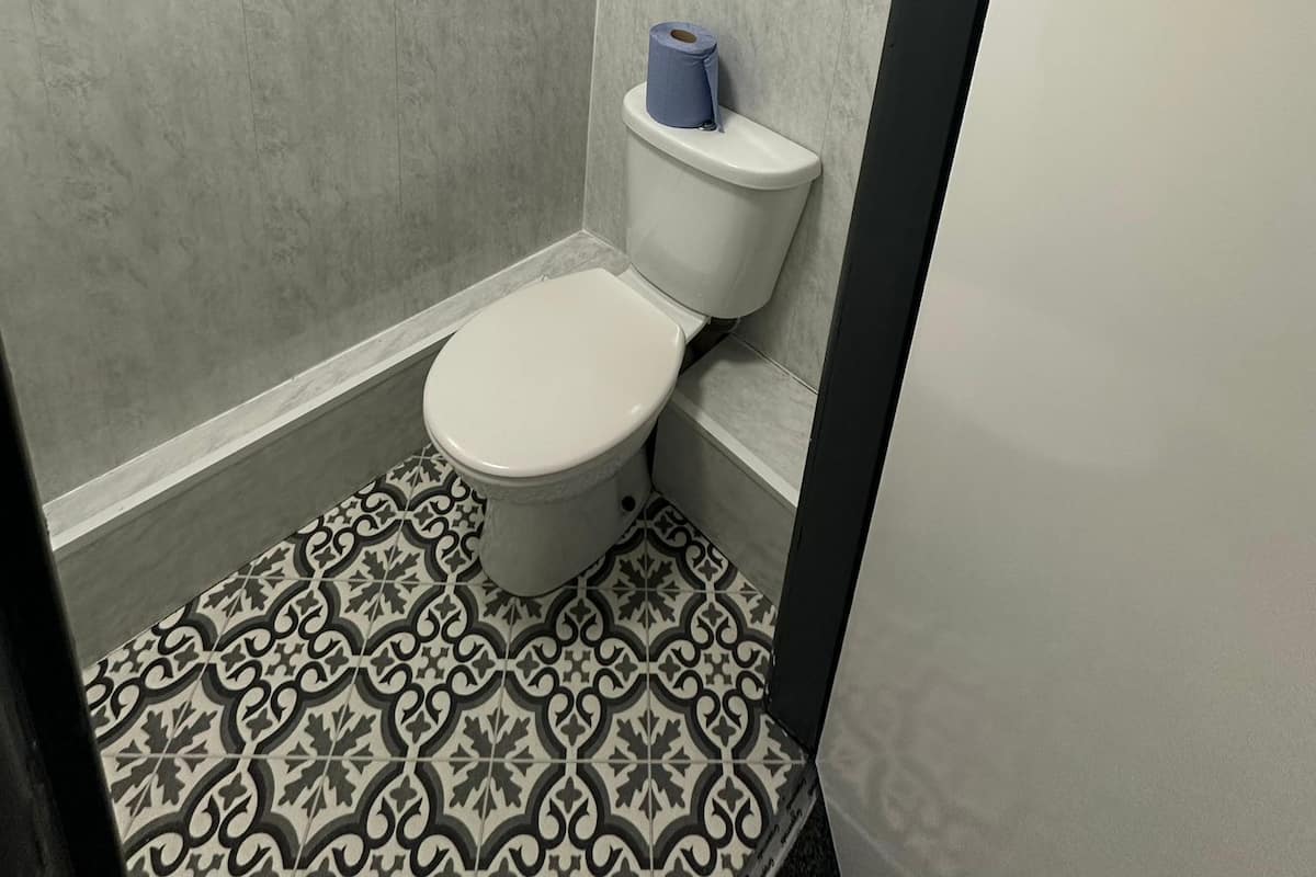 A small bathroom with a toilet, a roll of toilet paper, and patterned floor tiles.