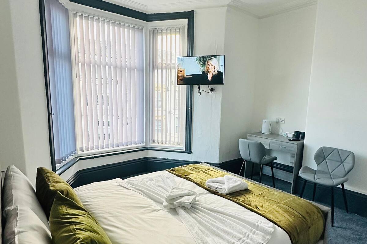 A hotel room with a large bed, a desk, a chair, and a television mounted on the wall.