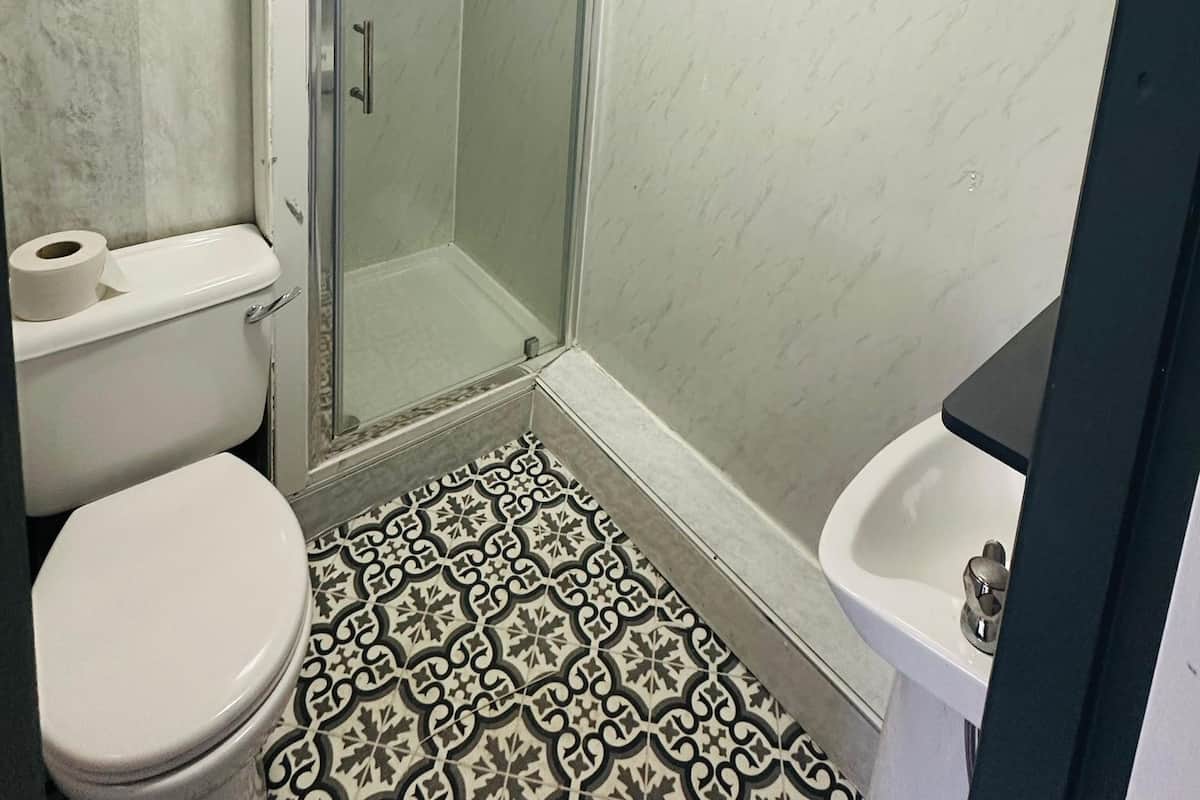 A bathroom with a toilet, a sink, a shower with a glass door, and patterned floor tiles.