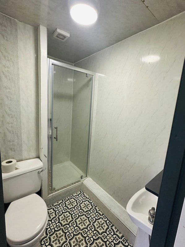 Un baño con inodoro, lavamanos, ducha con puerta de cristal y baldosas de suelo estampadas.