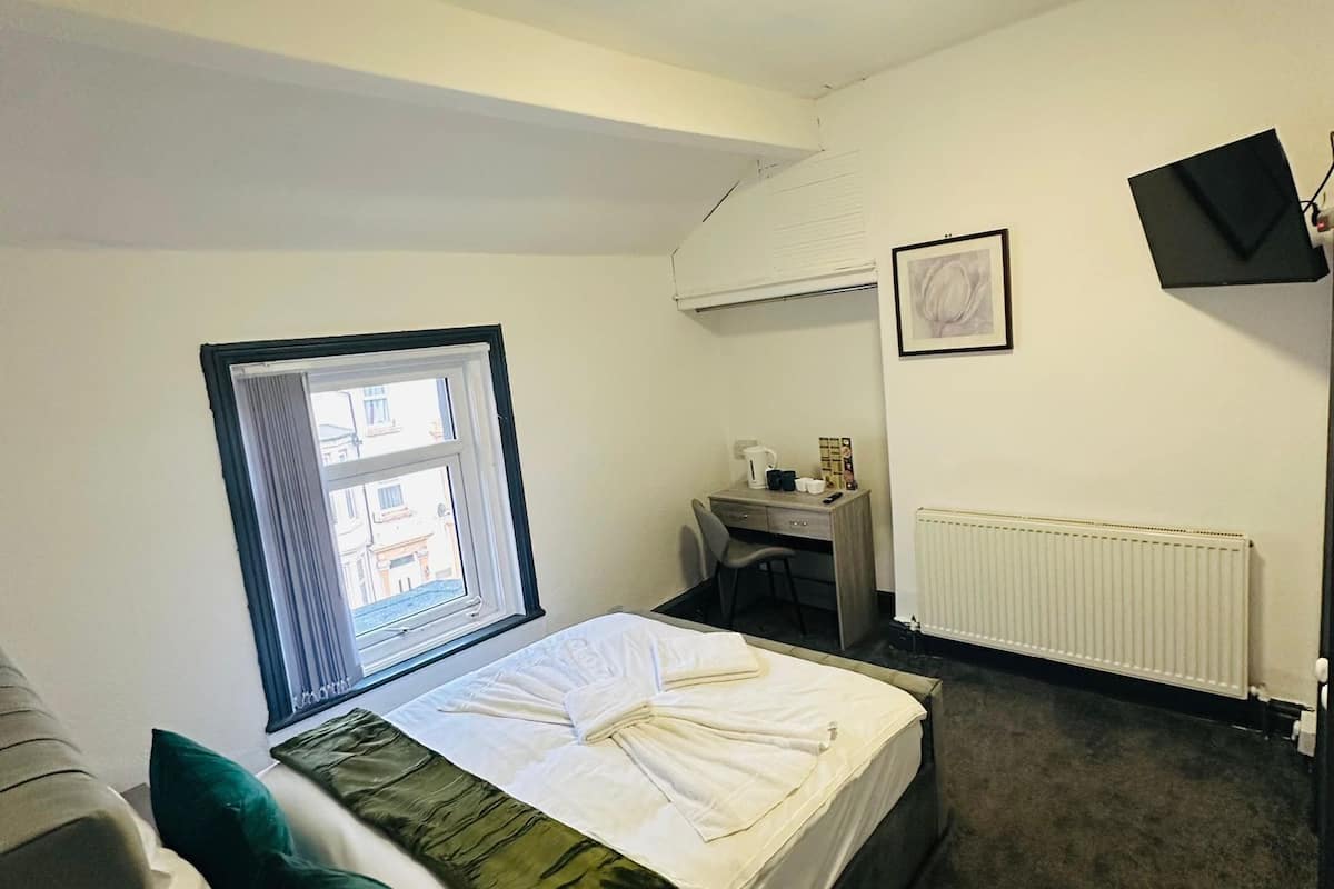 A bedroom with a bed, a desk, a chair, a radiator, and a window.