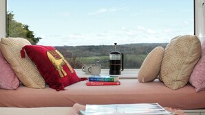 A cozy seating area with a view of a landscape, a coffee maker, and books on a windowsill.