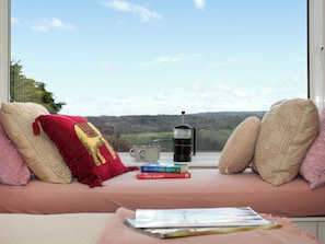 A cozy seating area with a view of a landscape, a coffee maker, and books on a windowsill.
