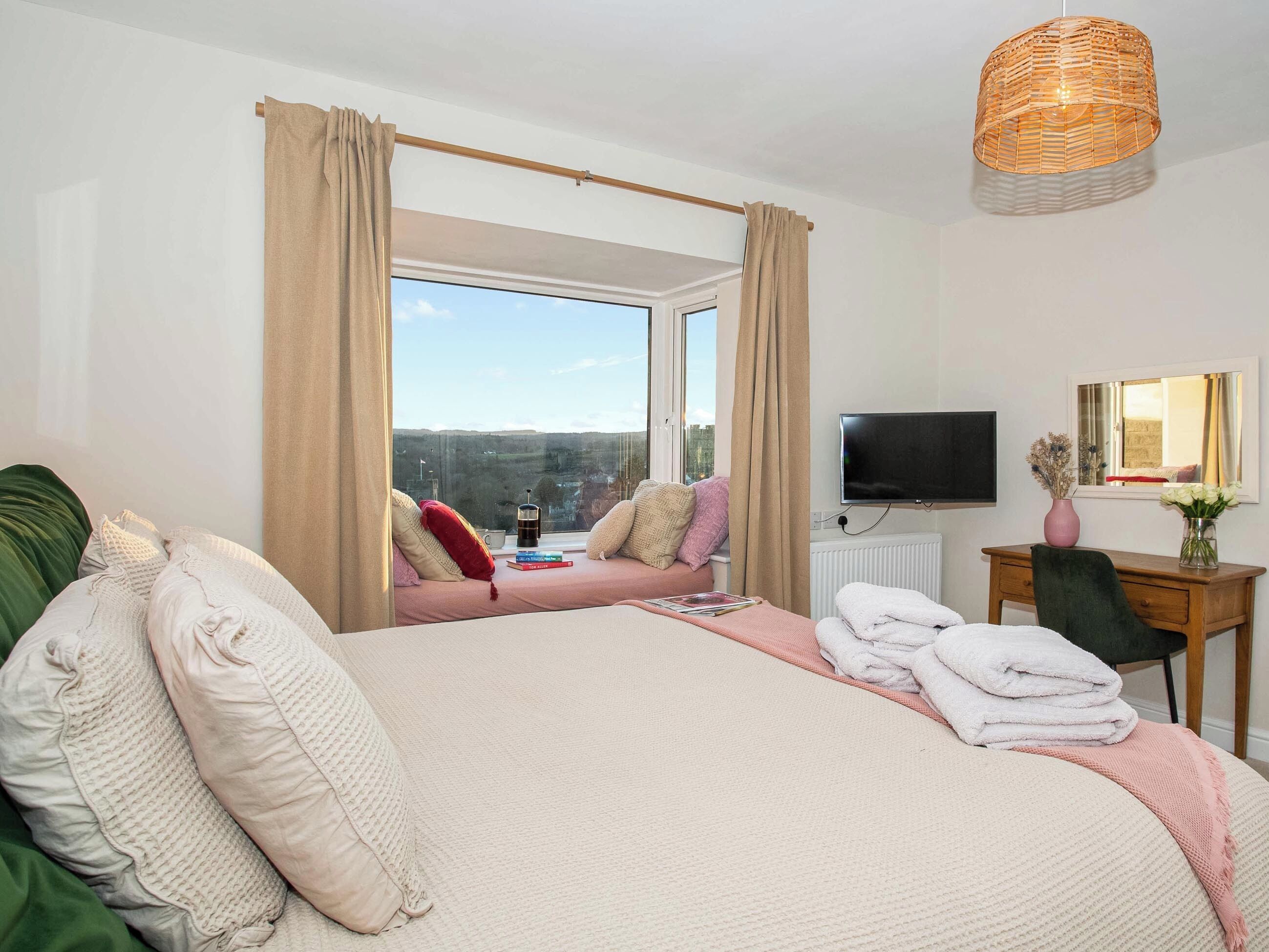 Een slaapkamer met een groot bed, een raam met gordijnen, een televisie, een bureau en een stoel.