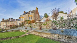 A residential area with stone walls, a grassy lawn, and houses with multiple windows.