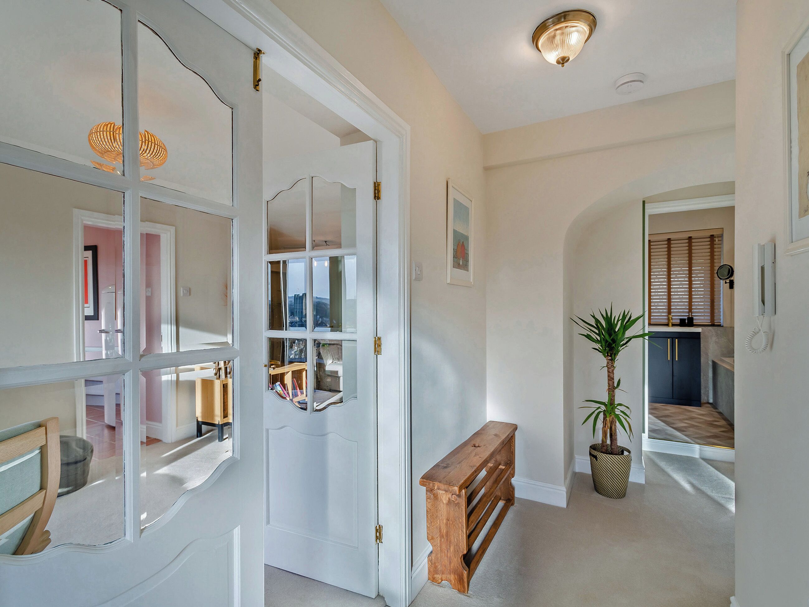 A hallway with a white door, a wooden bench, a potted plant, and a framed picture on the wall.