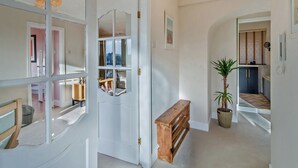 A hallway with a white door, a wooden bench, a potted plant, and a framed picture on the wall.