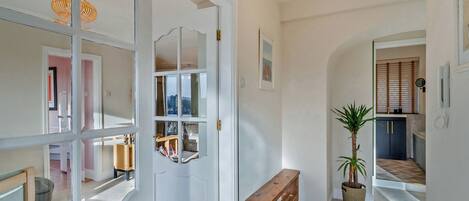 A hallway with a white door, a wooden bench, a potted plant, and a framed picture on the wall.