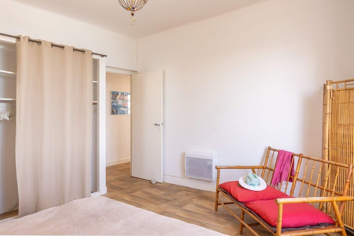 A room with a bed, a wooden chair with a red cushion, a white door, and a window with a view.
