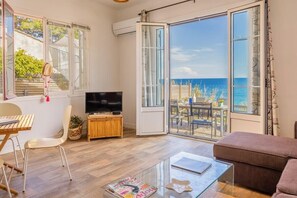 Una sala de estar con televisión, una mesa de centro de vidrio, un sofá y vista al mar a través de ventanas amplias.
