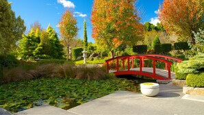 Un jardín tranquilo con un puente rojo, abundante vegetación y un estanque con nenúfares.