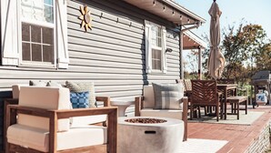 Une terrasse dotée de mobilier d’extérieur, d’un foyer et d’une maison ornée d’un motif solaire.
