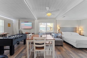 A room with a foosball table, a sofa, a bed, a TV, and a ceiling fan.