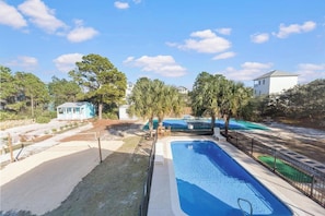 A swimming pool with a fenced deck, palm trees, and a small building in the background.