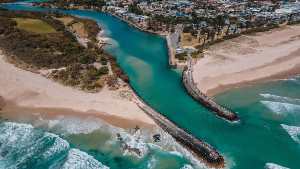 Vista aérea de una zona costera con un canal sinuoso, playas de arena y una densa área residencial con casas y edificios.