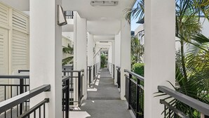 A corridor with white walls, black railings, and a grey floor leading to a door at the end. - Paradiso 3 Bedroom Family 230 (Kingscliff)