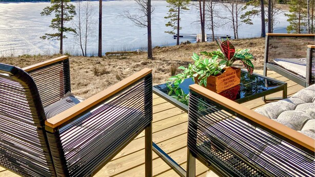 Une terrasse avec deux chaises et une table, donnant sur un lac gelé, avec des arbres en arrière-plan.