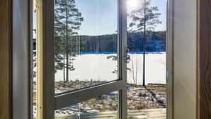 Une vue à travers une porte vitrée sur un paysage enneigé, avec des arbres et un ciel dégagé.