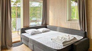 Un lit simple avec un matelas matelassé, une tête de lit rembourrée de couleur grise et une vue sur un lac par la fenêtre.