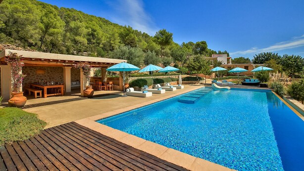 A pool area with lounge chairs and umbrellas, surrounded by greenery and stone structures. - Awesome home in Sant Antoni de Portman (Sant Antoni de Portman)