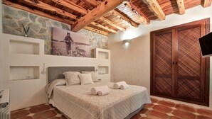 A bedroom with a stone wall, a wooden ceiling, a bed with a quilt, and a wardrobe with a lattice design. - Awesome home in Sant Antoni de Portman (Sant Antoni de Portman)