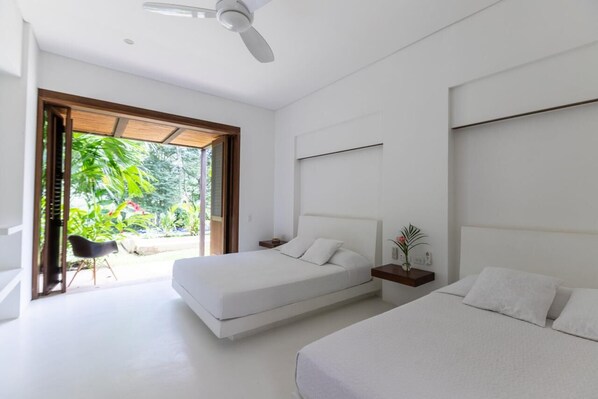 A modern bedroom with two beds, a ceiling fan, and a view of greenery outside.