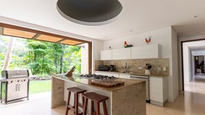 Una cocina moderna con una isla central, taburetes de bar, una parrilla empotrada y vistas al jardín.