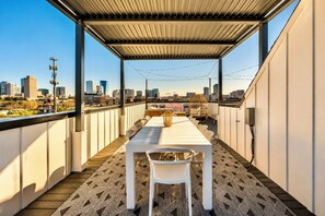A rooftop terrace with a dining table and chairs, a patterned floor, and a city skyline view.