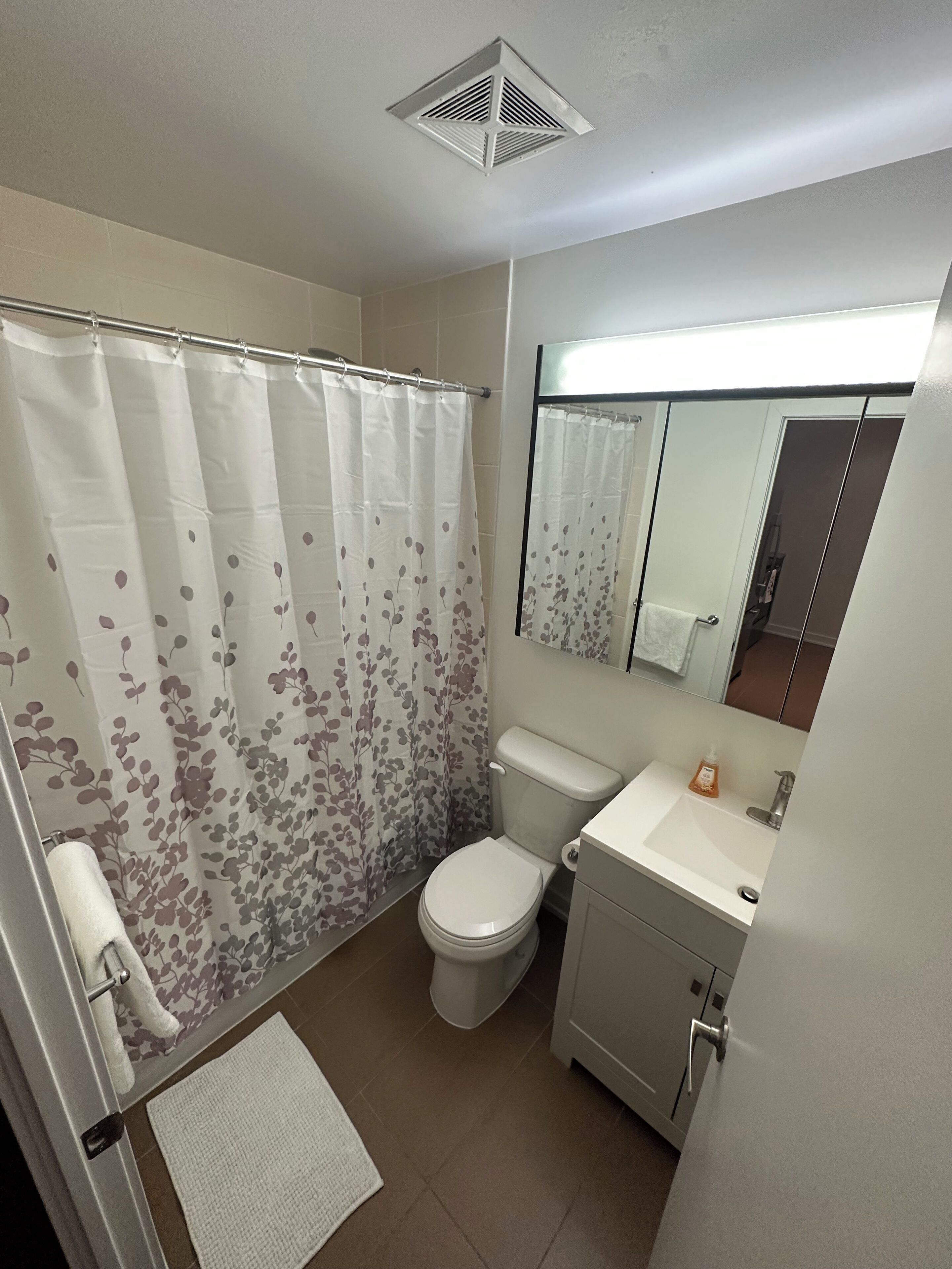 A bathroom with a shower curtain, toilet, sink, and a mirror above the sink.
