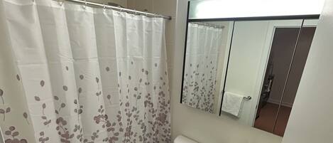 A bathroom with a shower curtain, toilet, sink, and a mirror above the sink.