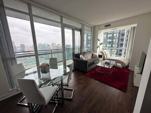 A modern living room with a glass coffee table, a grey sofa, and a red rug. - Beautiful 2Bed 2Bath Condo Steps to Square One  (Mississauga)