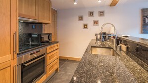 A modern kitchen with wooden cabinets, a stainless steel oven, a microwave, and a granite countertop. - Belvédère du Brévent - Welkeys (Chamonix-Mont-Blanc)