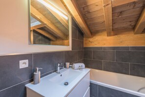 A modern bathroom with a white sink, mirror, and bathtub. - Belvédère du Brévent - Welkeys (Chamonix-Mont-Blanc)