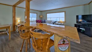 Un vaste espace de vie comprenant une table à manger en bois, quatre chaises en bois, un canapé, un téléviseur et une grande fenêtre.