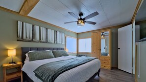 Une chambre à coucher comprenant un lit, une table de chevet, un ventilateur de plafond, une fenêtre et une armoire.